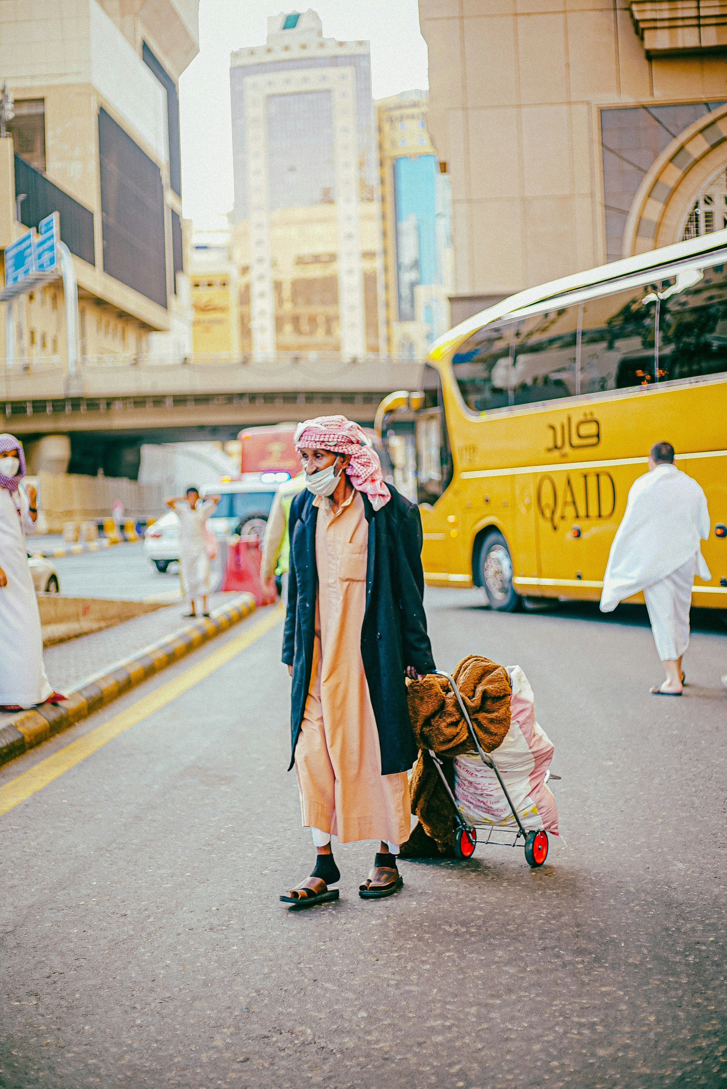 A traveller pulling a loaded luggage trolley past a pilgrim coach on a Makkah street
