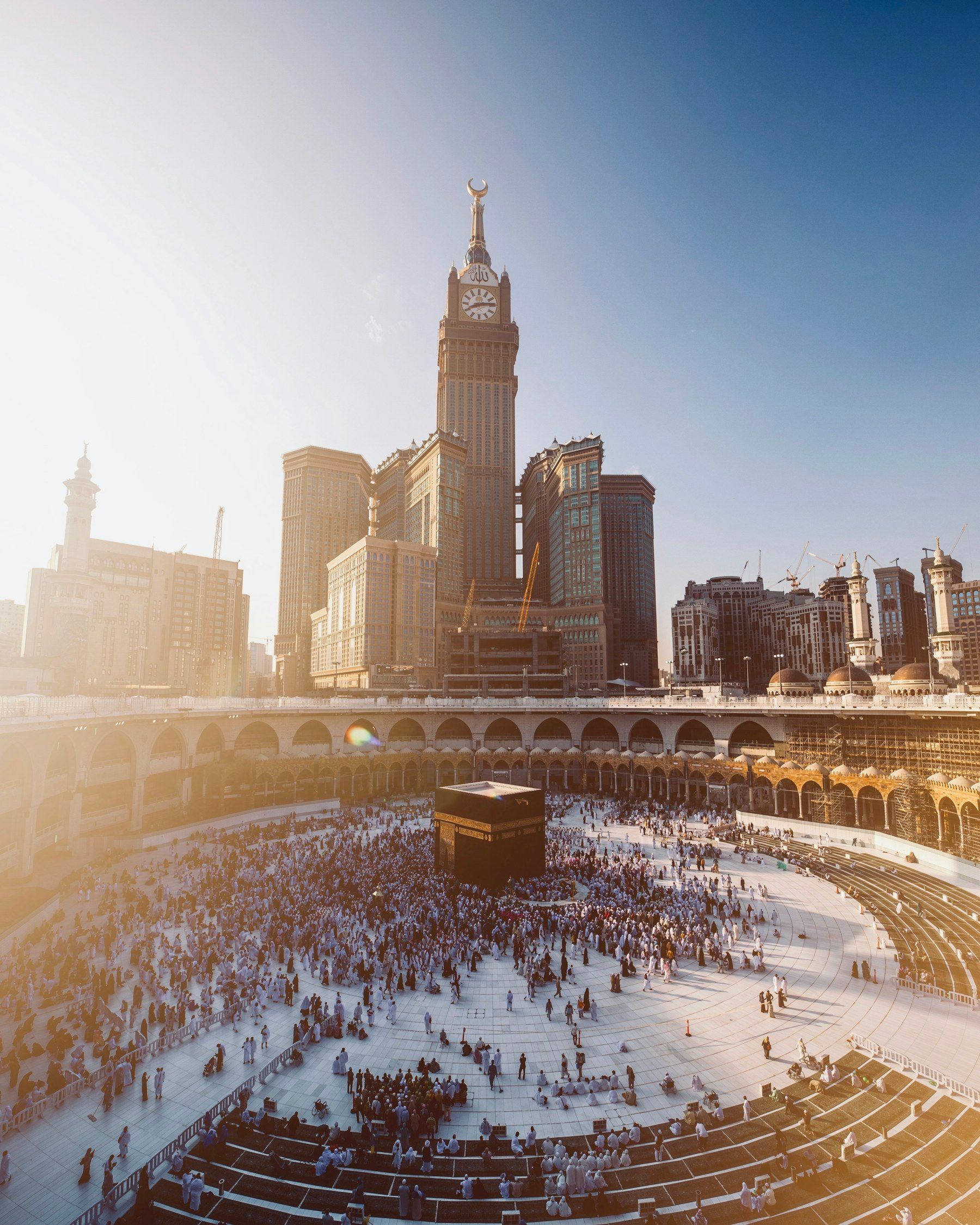 Pilgrims circling the Kaaba in Masjid al-Haram at sunrise, with the Makkah hotel towers behind