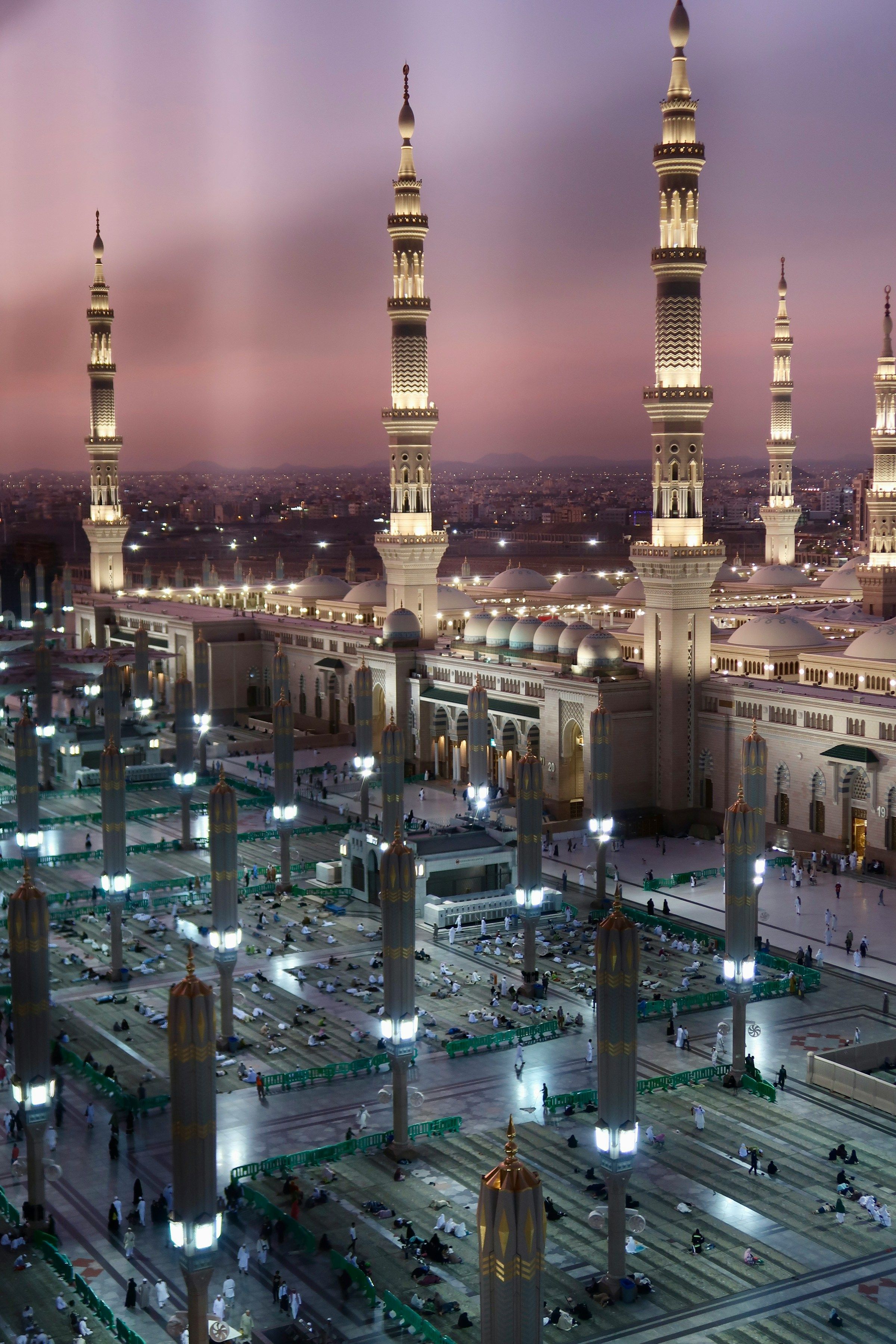 Al-Masjid an-Nabawi and the Madinah skyline lit at dusk, with pilgrims resting in the courtyard